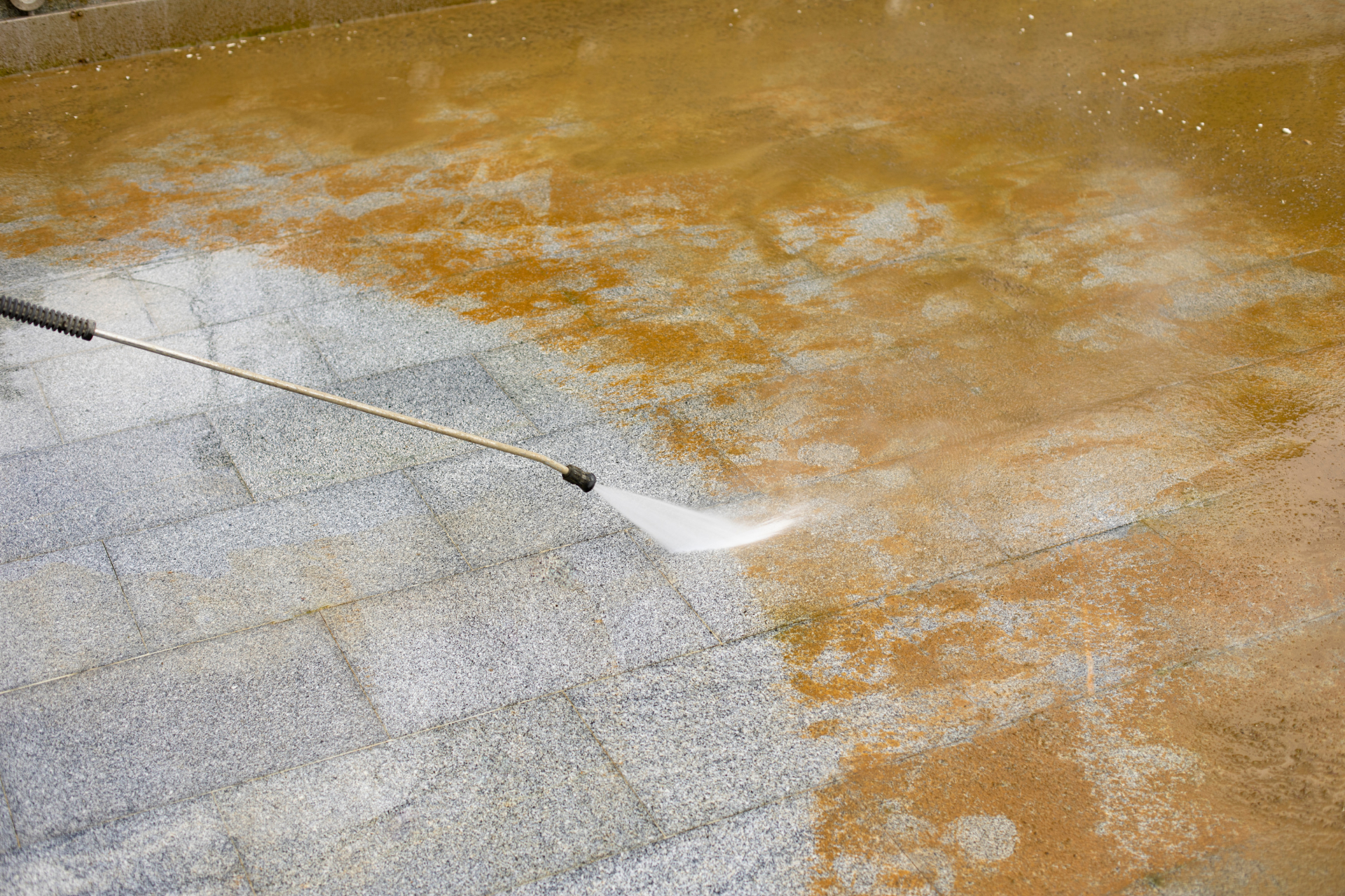 Pressure washing a wet stone patio, with a spray nozzle cleaning orange-stained tiles