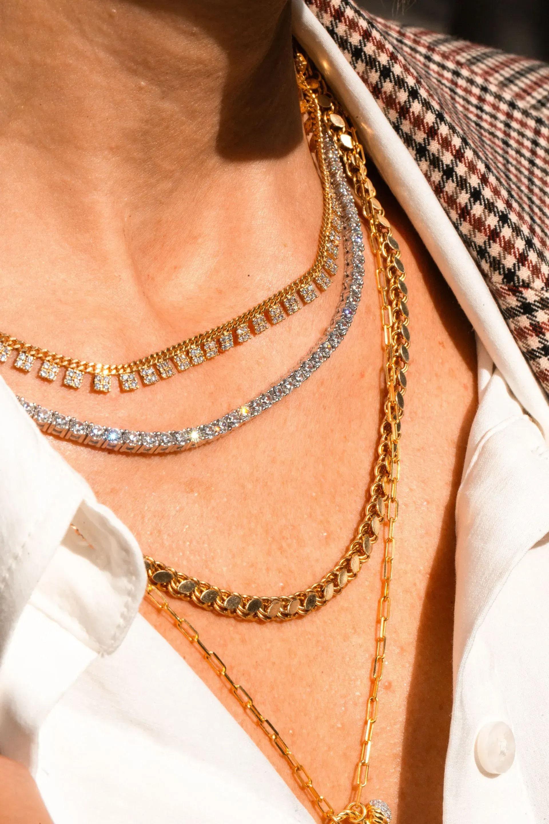 Close-up of layered gold and silver chain necklaces on a person in a white shirt and checkered jacket
