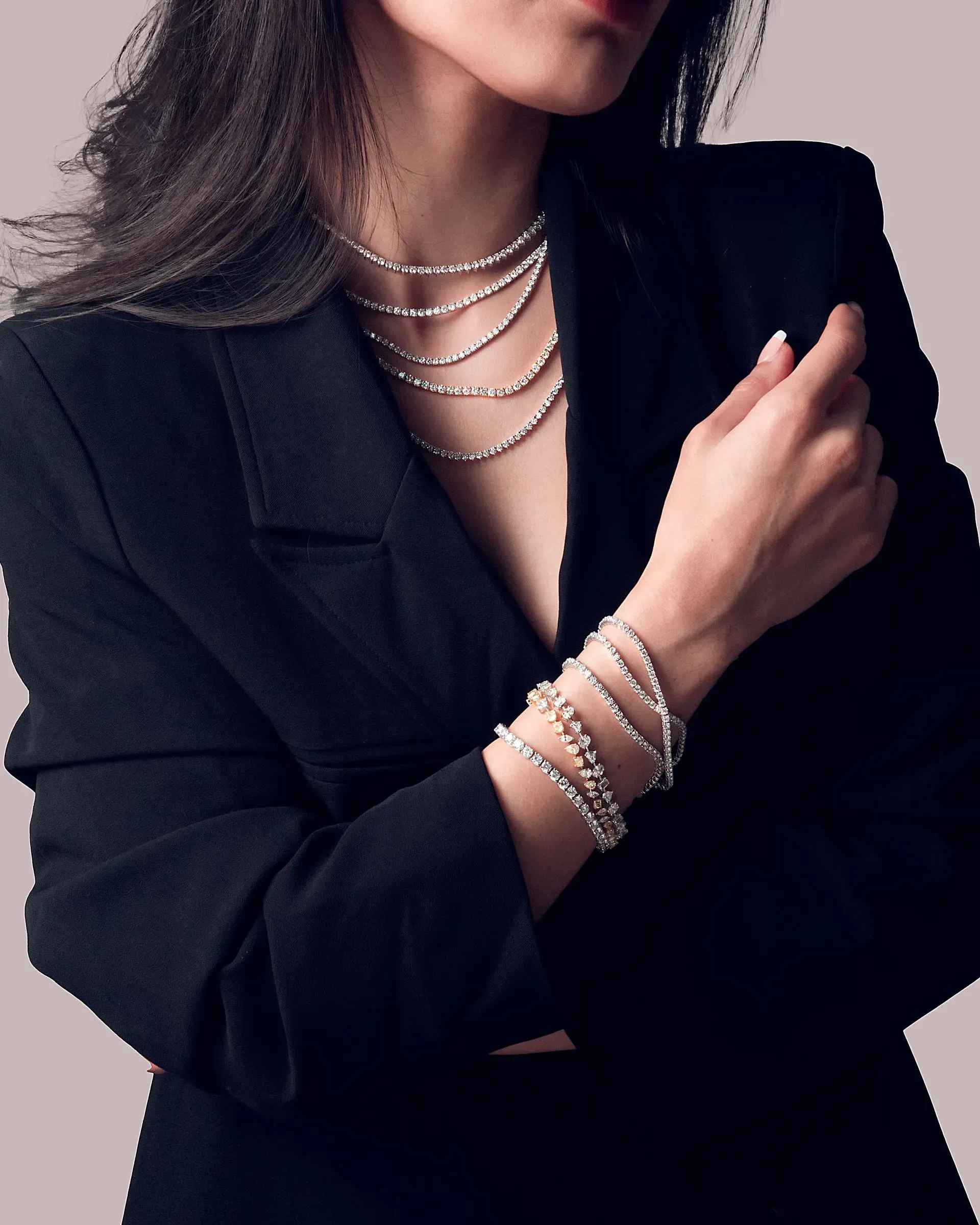 Woman in a black blazer wearing layered silver necklaces and bracelets, cropped from shoulders to waist.