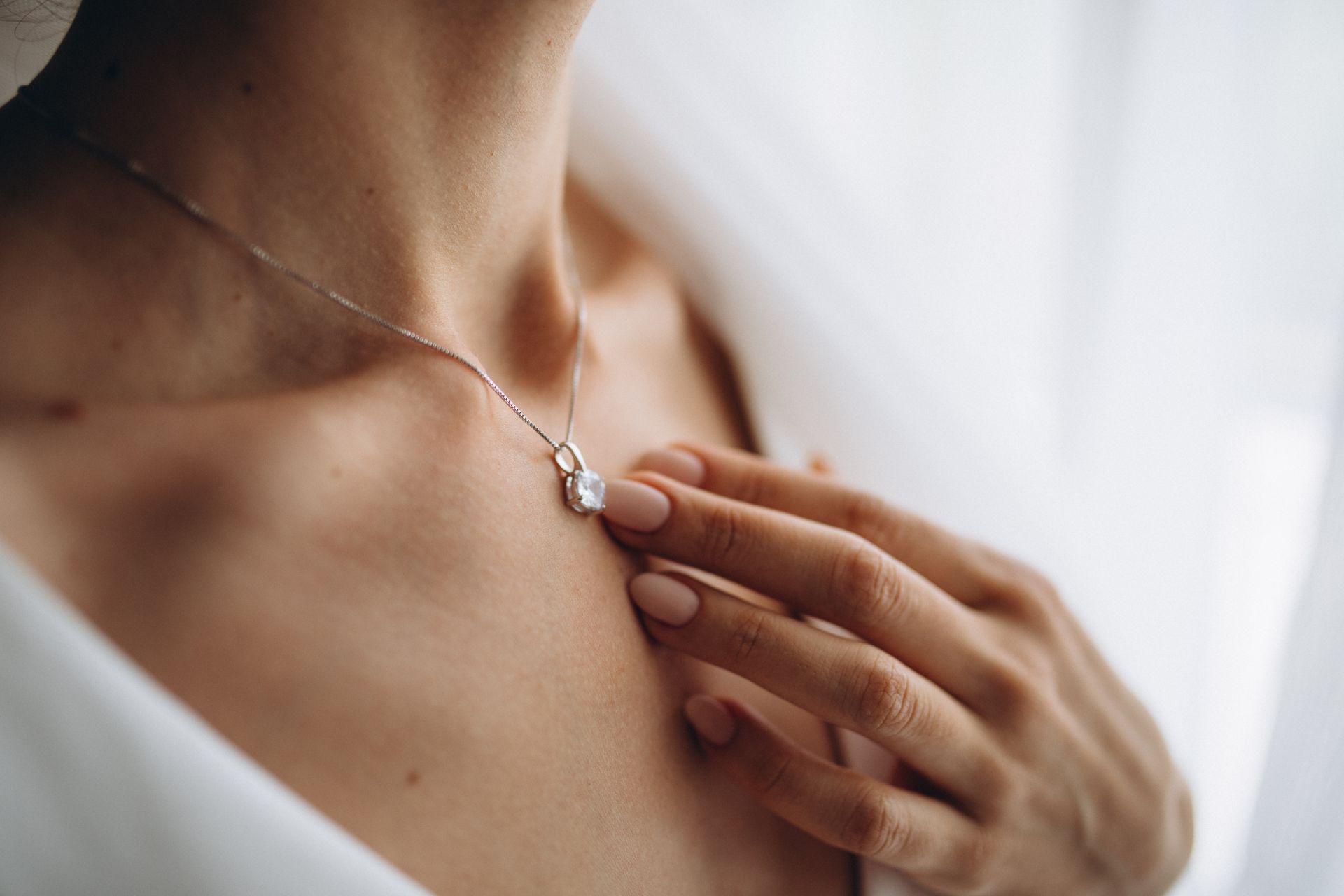 Hand touching a silver pendant necklace on a neck, near a bright window