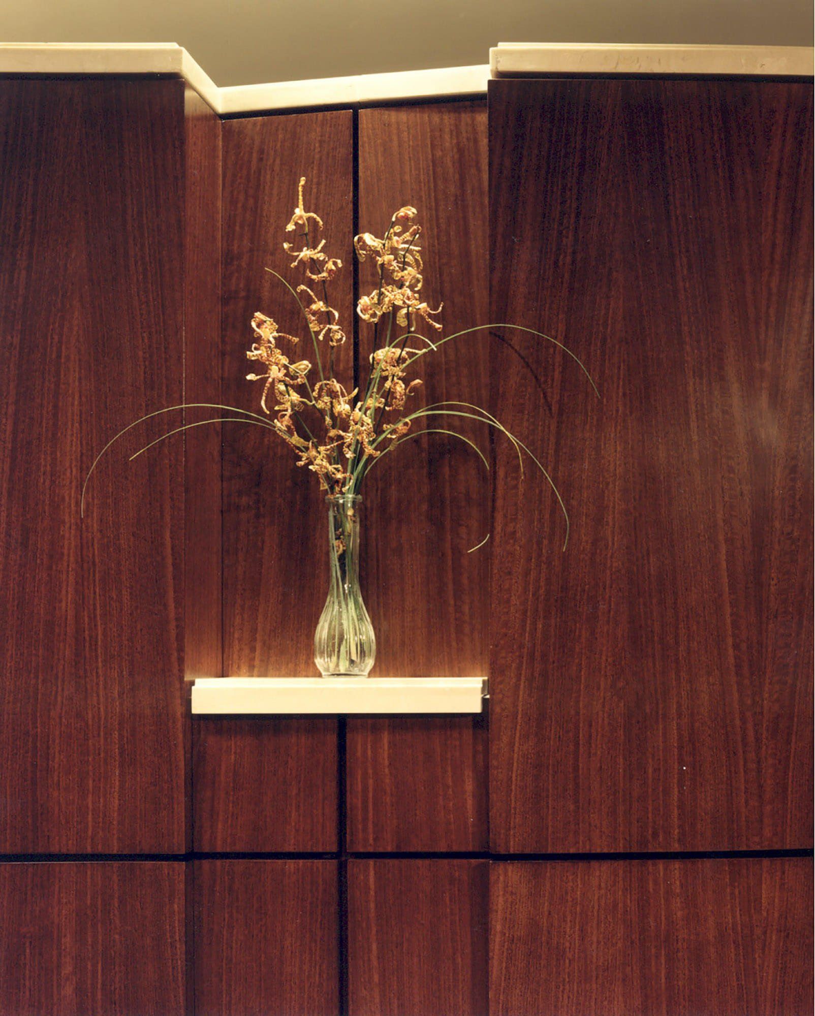 a vase of flowers sits on a shelf in front of a wooden wall