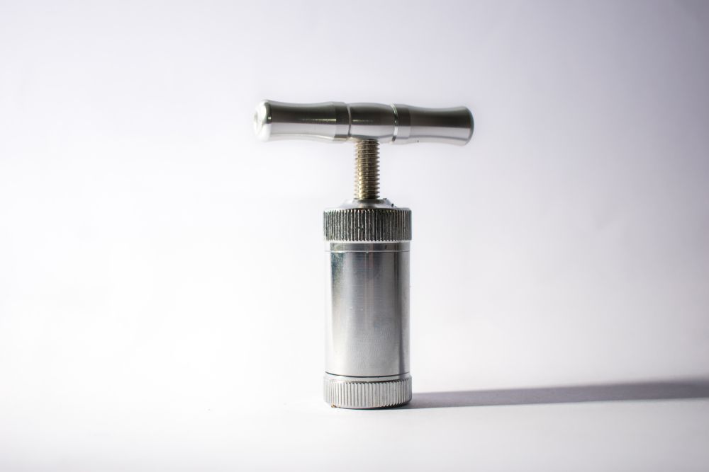 A silver metal object with a t-shaped handle is sitting on a white surface.
