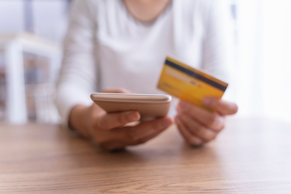 A woman is holding a credit card and a cell phone.