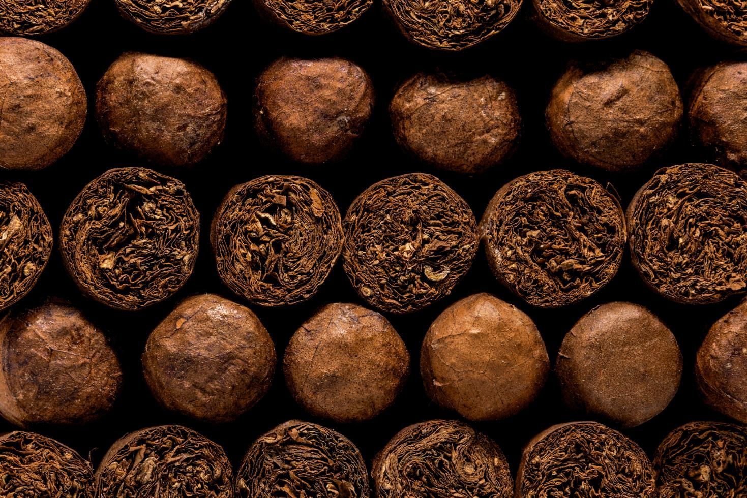 Cigars in a wooden box beside a glass of amber liquor on a dark table