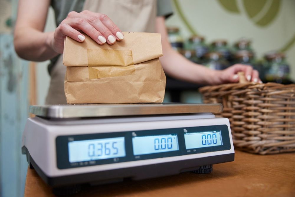 A woman is weighing a bag of food on a scale.