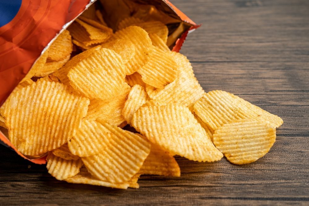 A bag of potato chips is spilled on a wooden table.