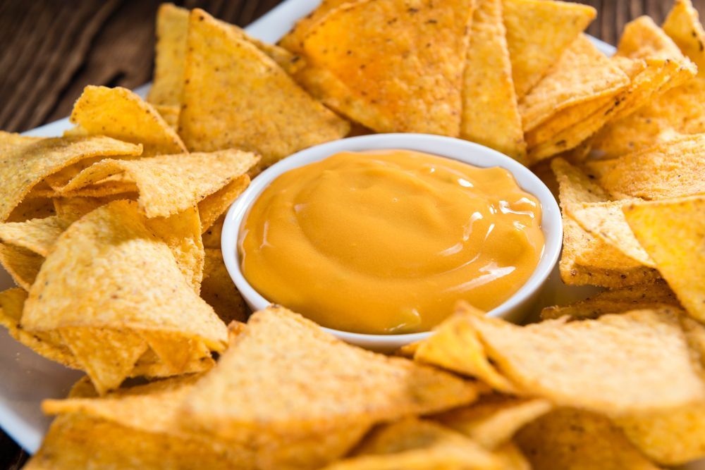 A plate of nachos with a bowl of cheese sauce on a wooden table.