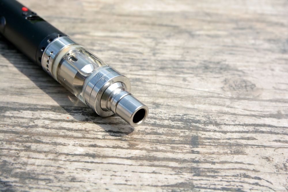 Close-up of a vape pen with a black body and silver mouthpiece on a wooden surface