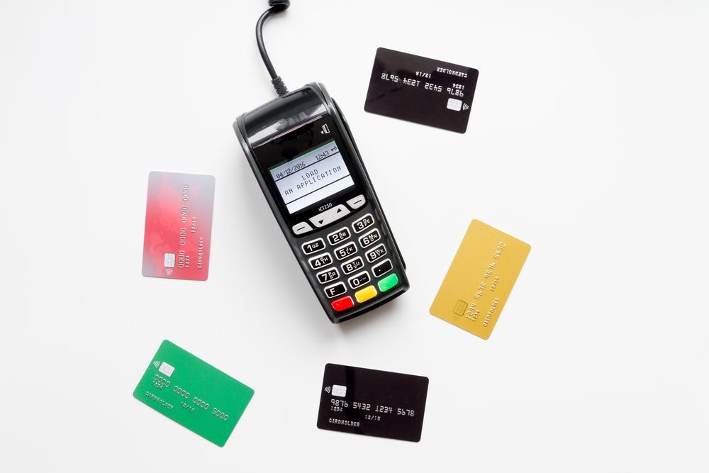 A credit card machine is surrounded by credit cards on a white surface.