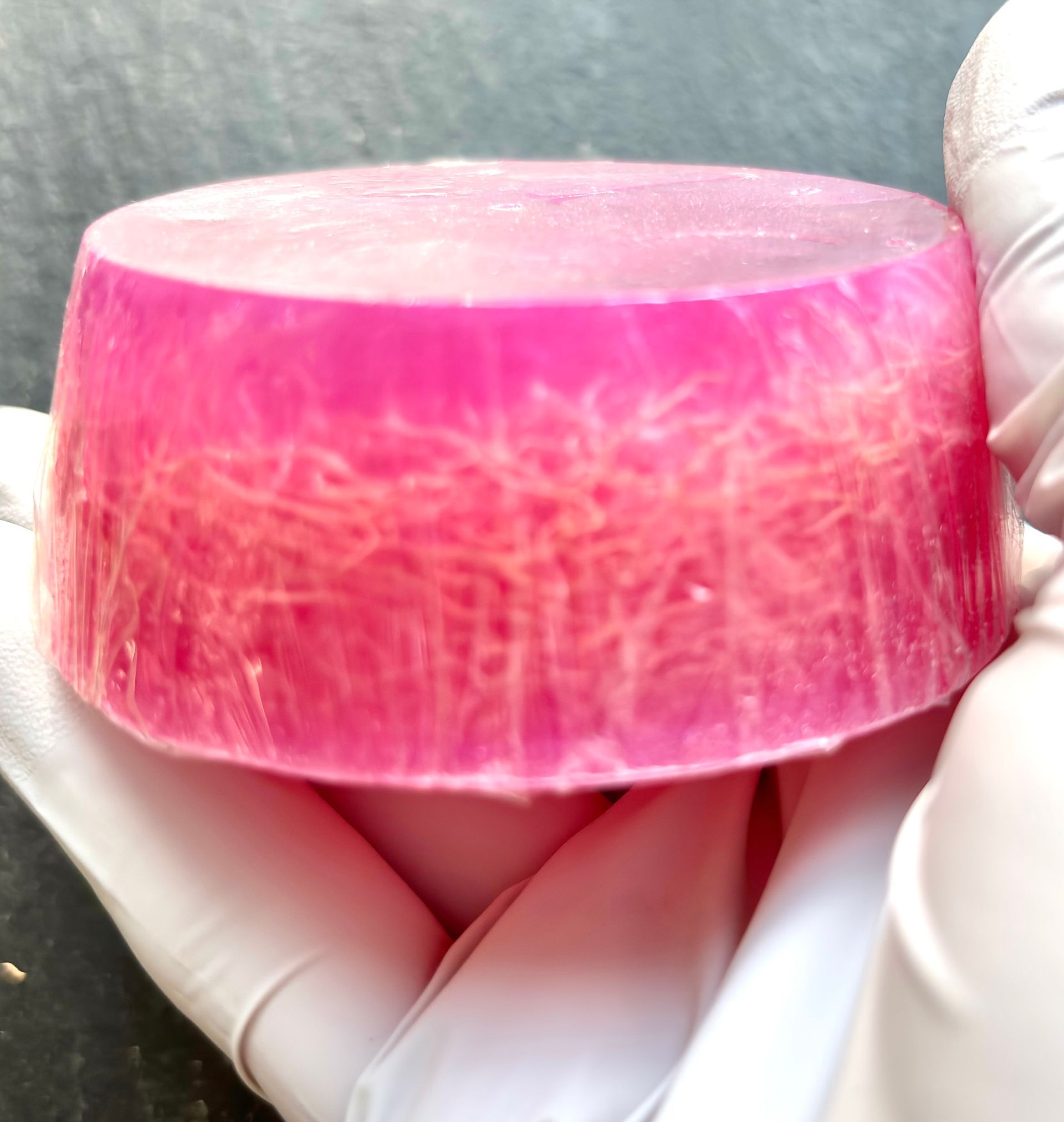 A person wearing white gloves is holding a pink soap bar