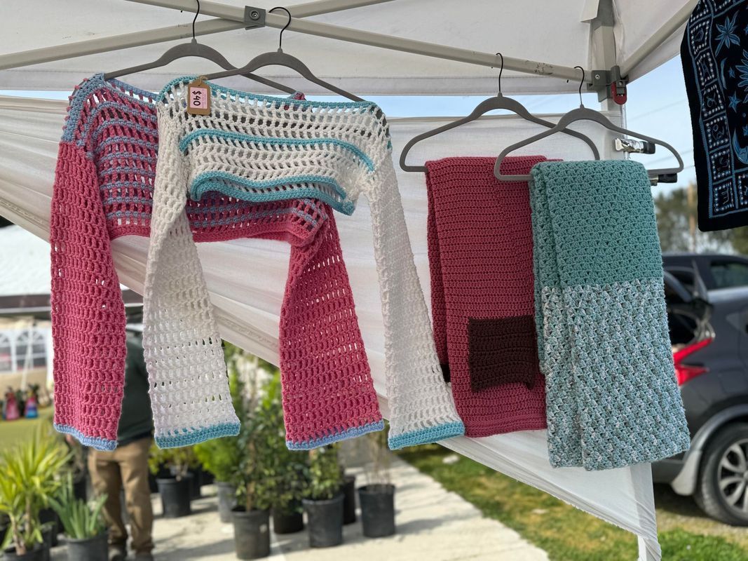 A bunch of crocheted sweaters are hanging on a hanger.
