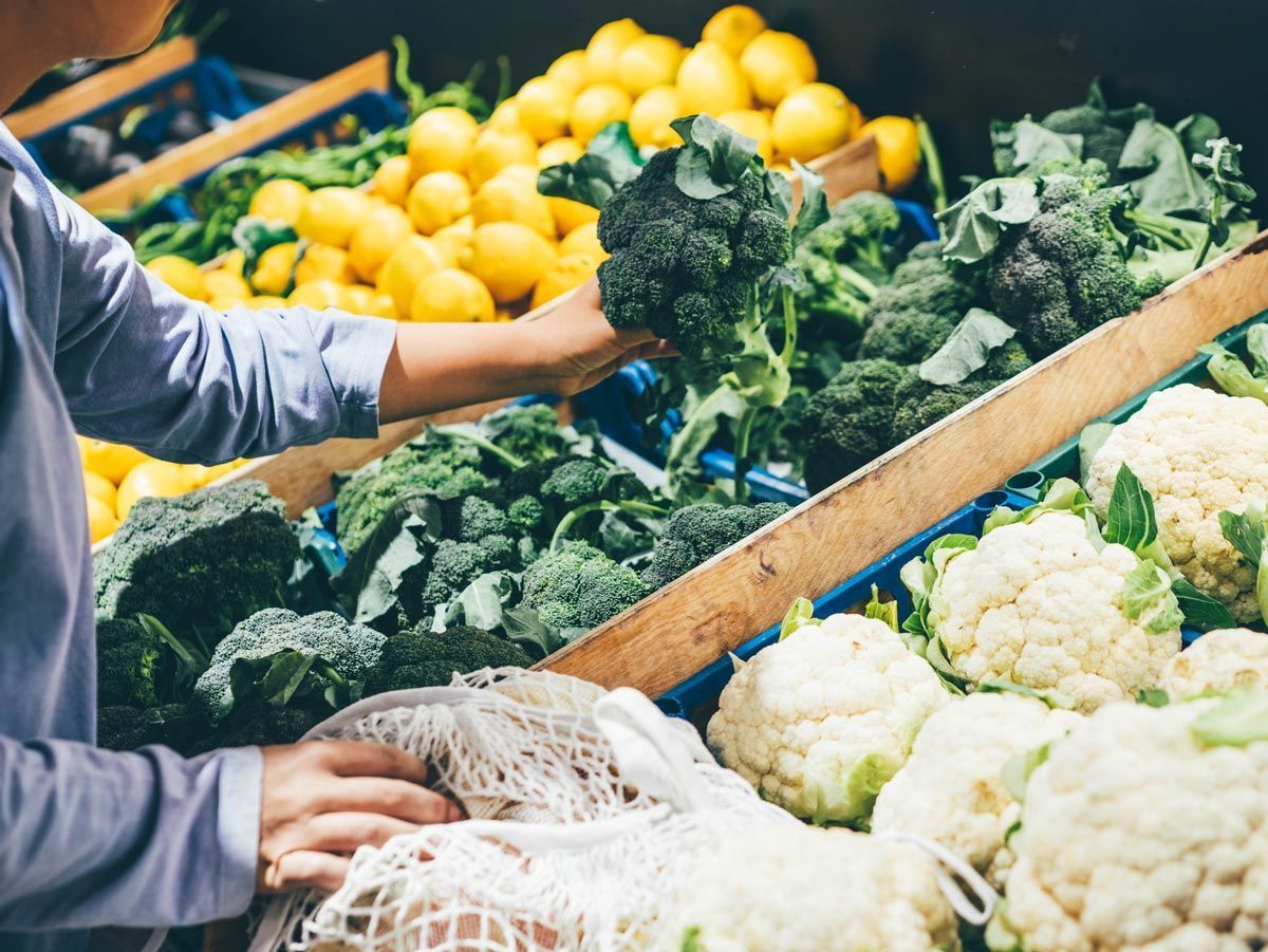 A person is picking broccoli and cauliflower at a market.
