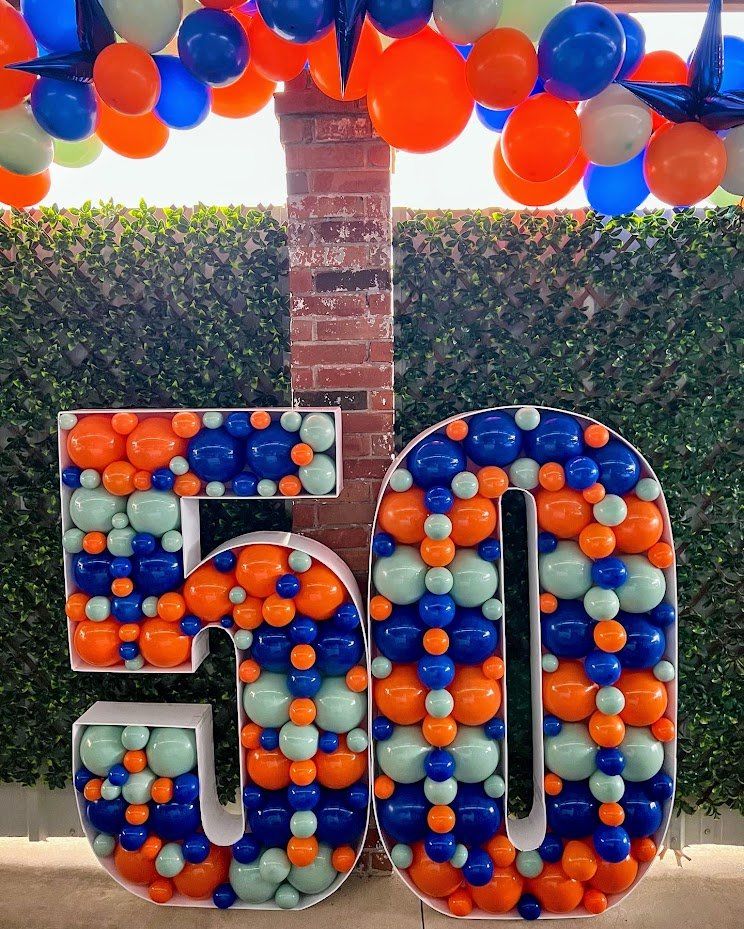 A large number 50 made of balloons is sitting in front of a brick wall.