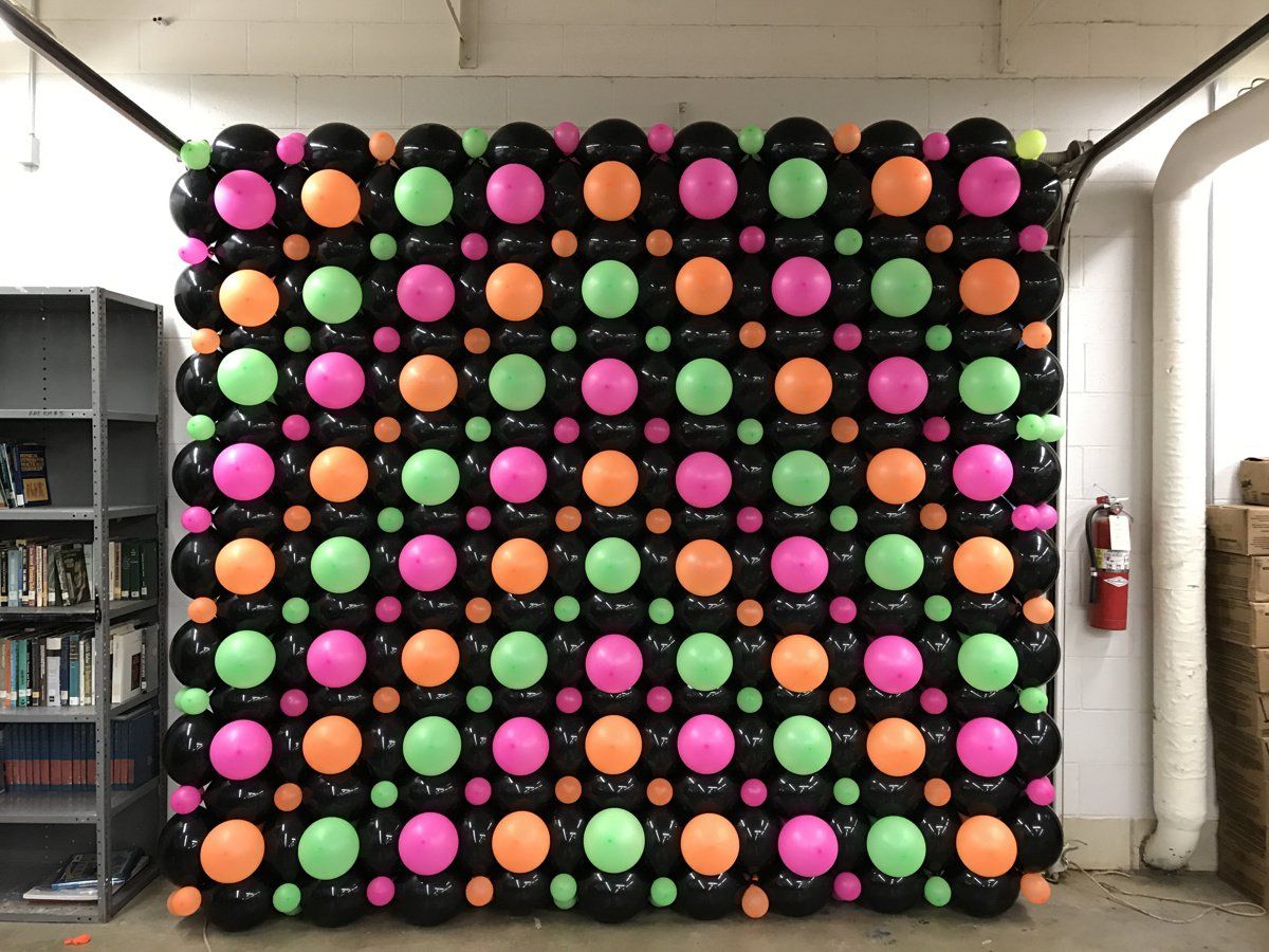 A wall of colorful balloons in a room with a fire extinguisher.