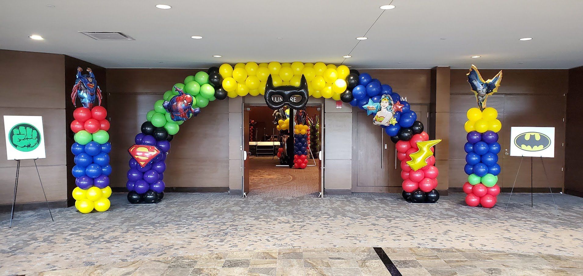 A room with a balloon arch decorated with superhero balloons.