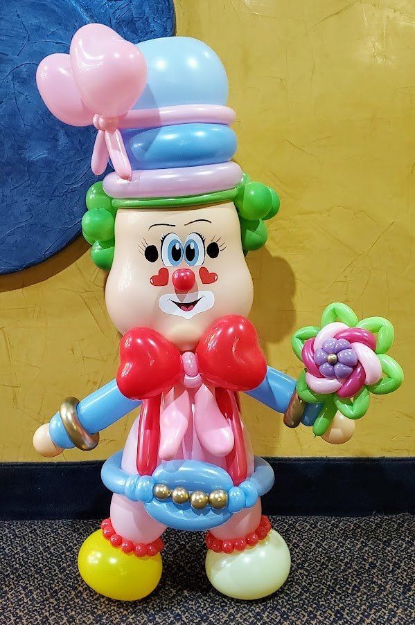 A clown made out of balloons is holding a flower and a balloon.