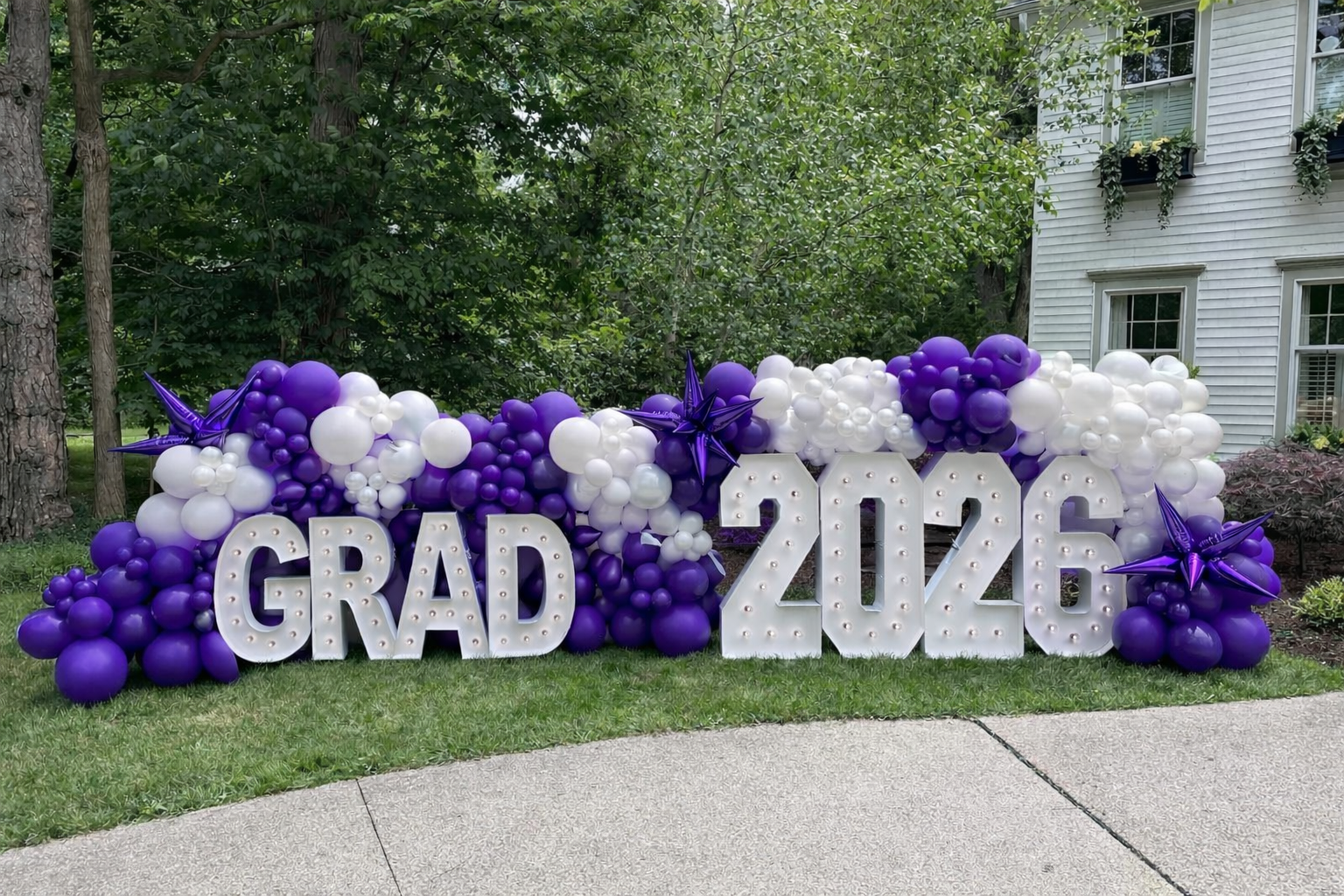 Festive 2026 GRAD illuminated marquee letters balloon display. Purple, white, star balloons.