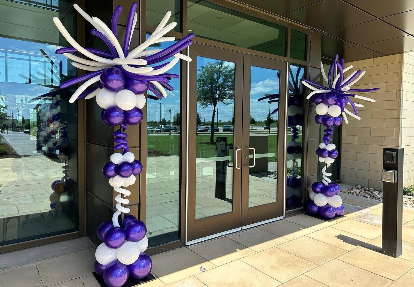 Purple and white school color balloon columns outside of an entrace.