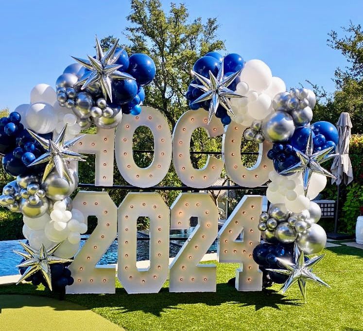 Large balloon garland featuring illuminated marquee numbers and blue, silver, and white balloons for a school celebration