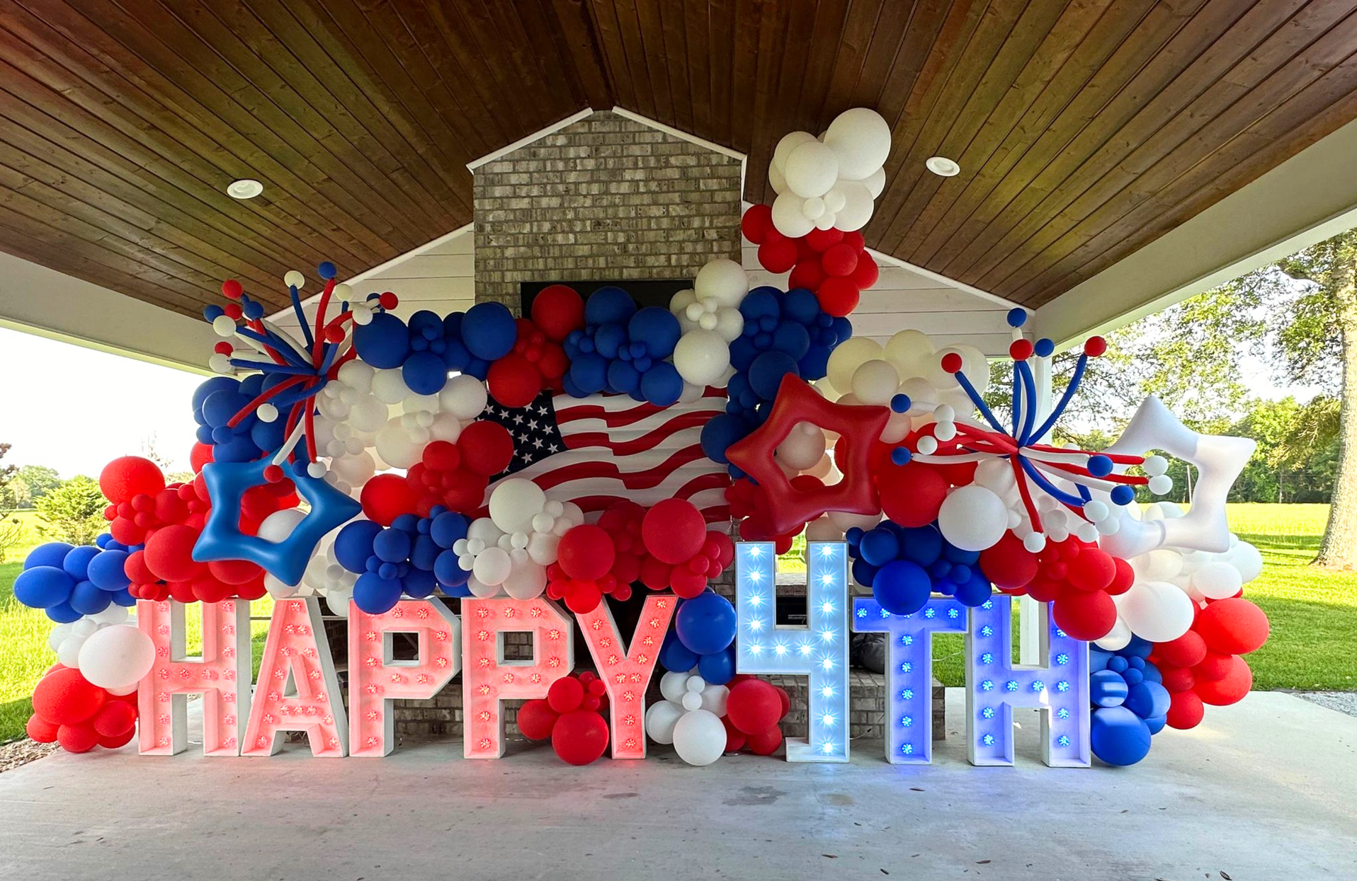 Massive patriotic 4th of July balloon installation: red, white, blue organic garland, 'HAPPY 4TH' marquee letters.
