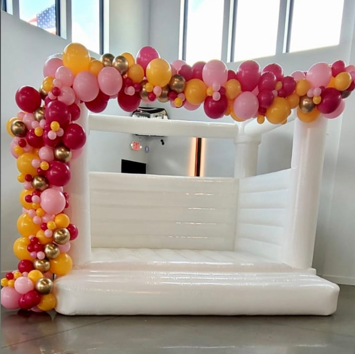A white bouncy castle is decorated with pink and yellow balloons