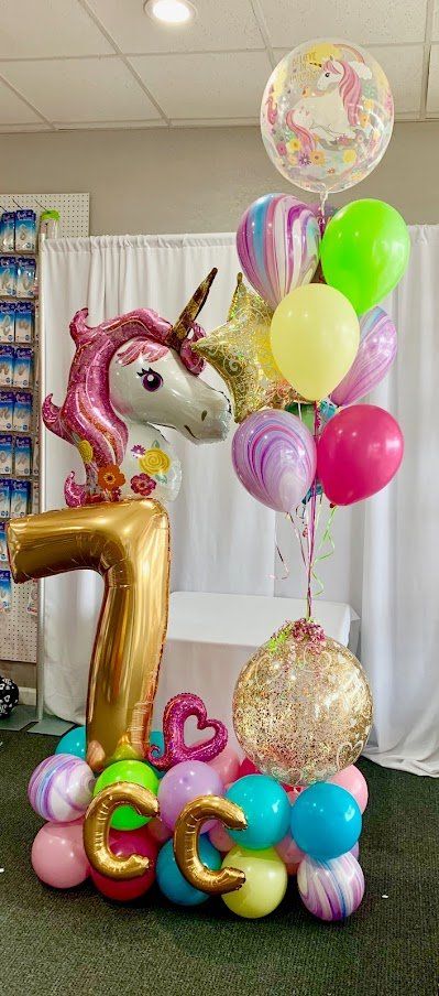 A bunch of balloons and a unicorn balloon are sitting on top of a table.