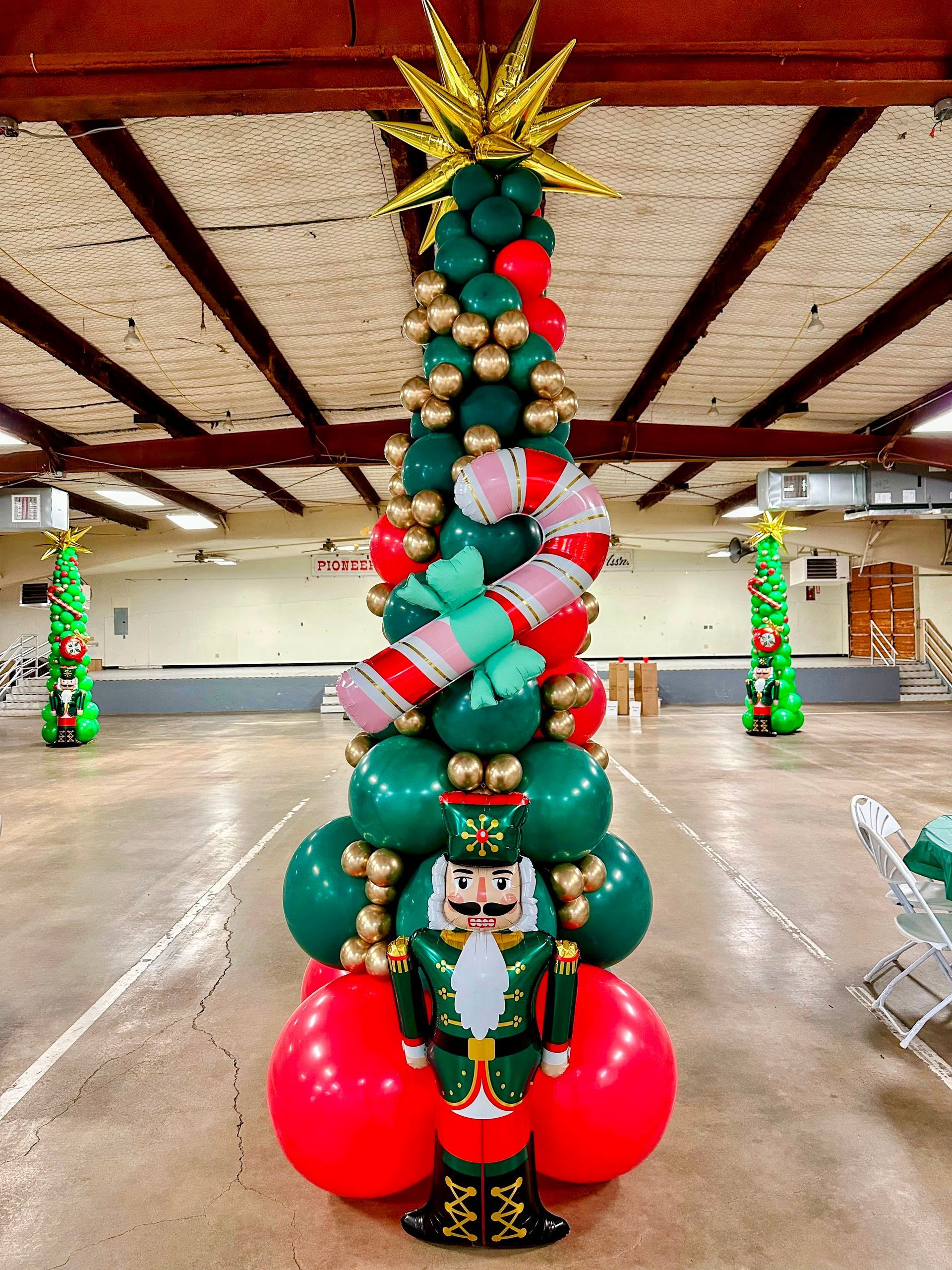 Tall balloon sculpture of a Christmas tree with green, gold and red balloons and a candy cane balloon accent