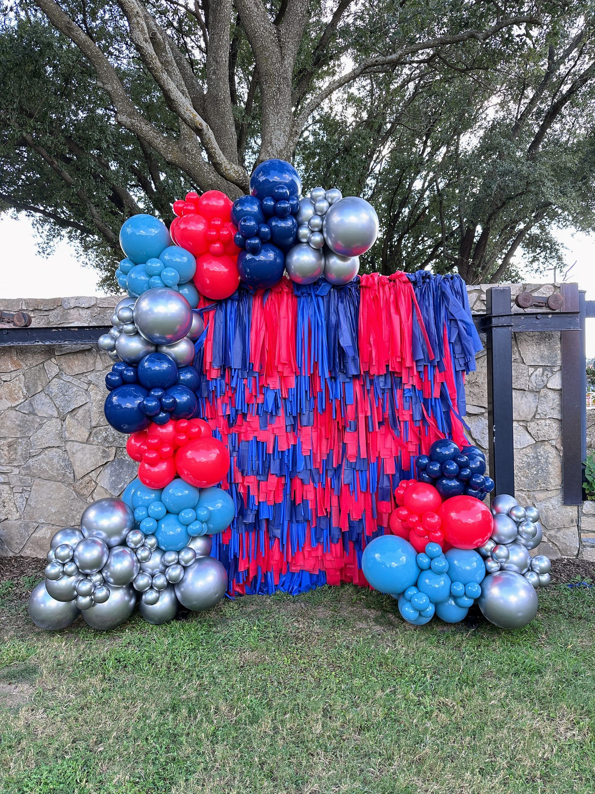 School spirit balloon garland styled with red, blue, and silver balloons on a streamer wall backdrop