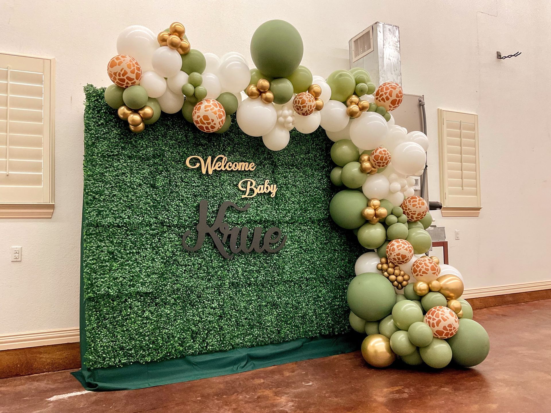 A green and white balloon arch is sitting in front of a green wall.