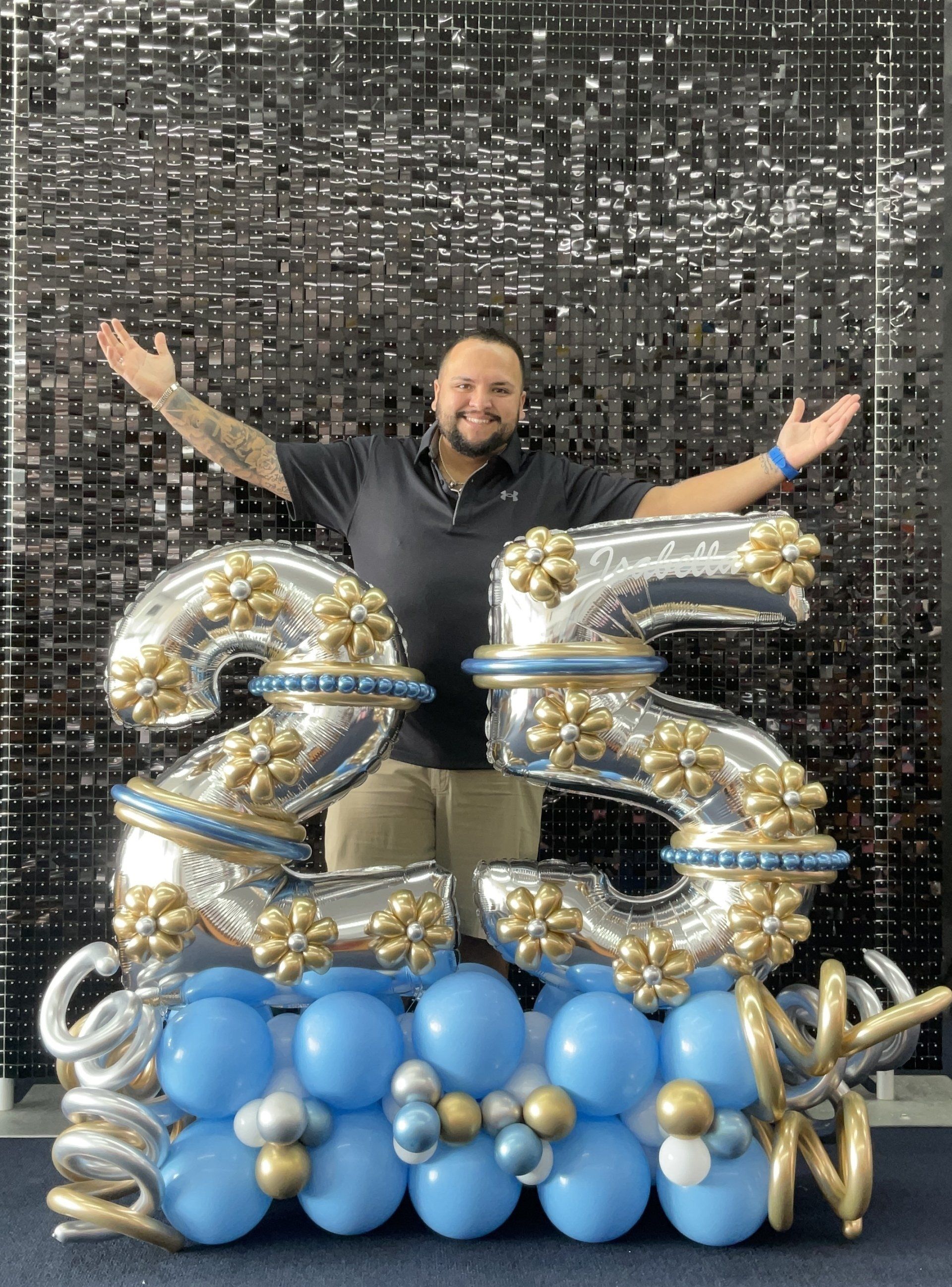 A man is standing in front of a large number 25 made of balloons.