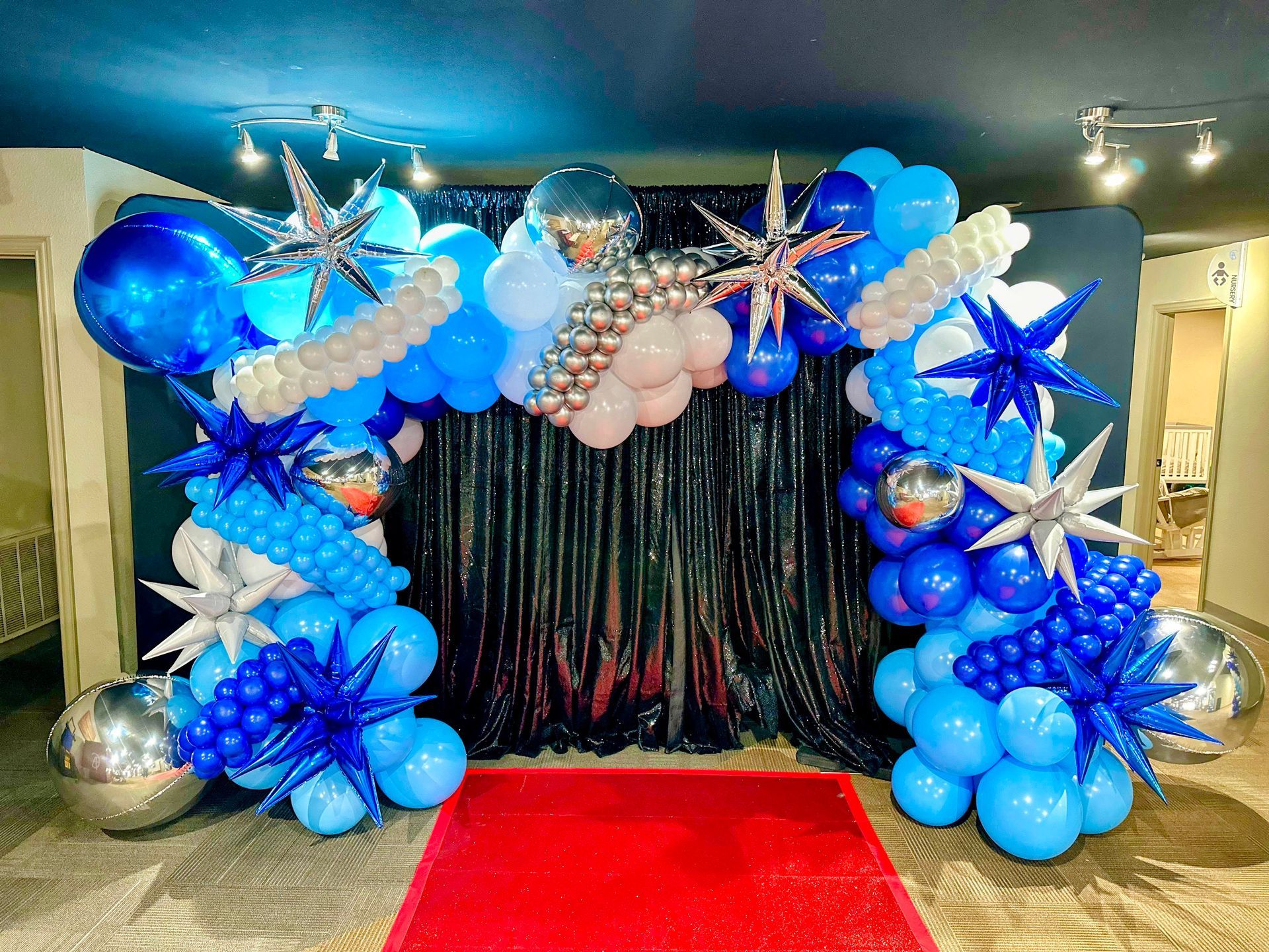 A room decorated with blue and silver balloons and a red carpet.