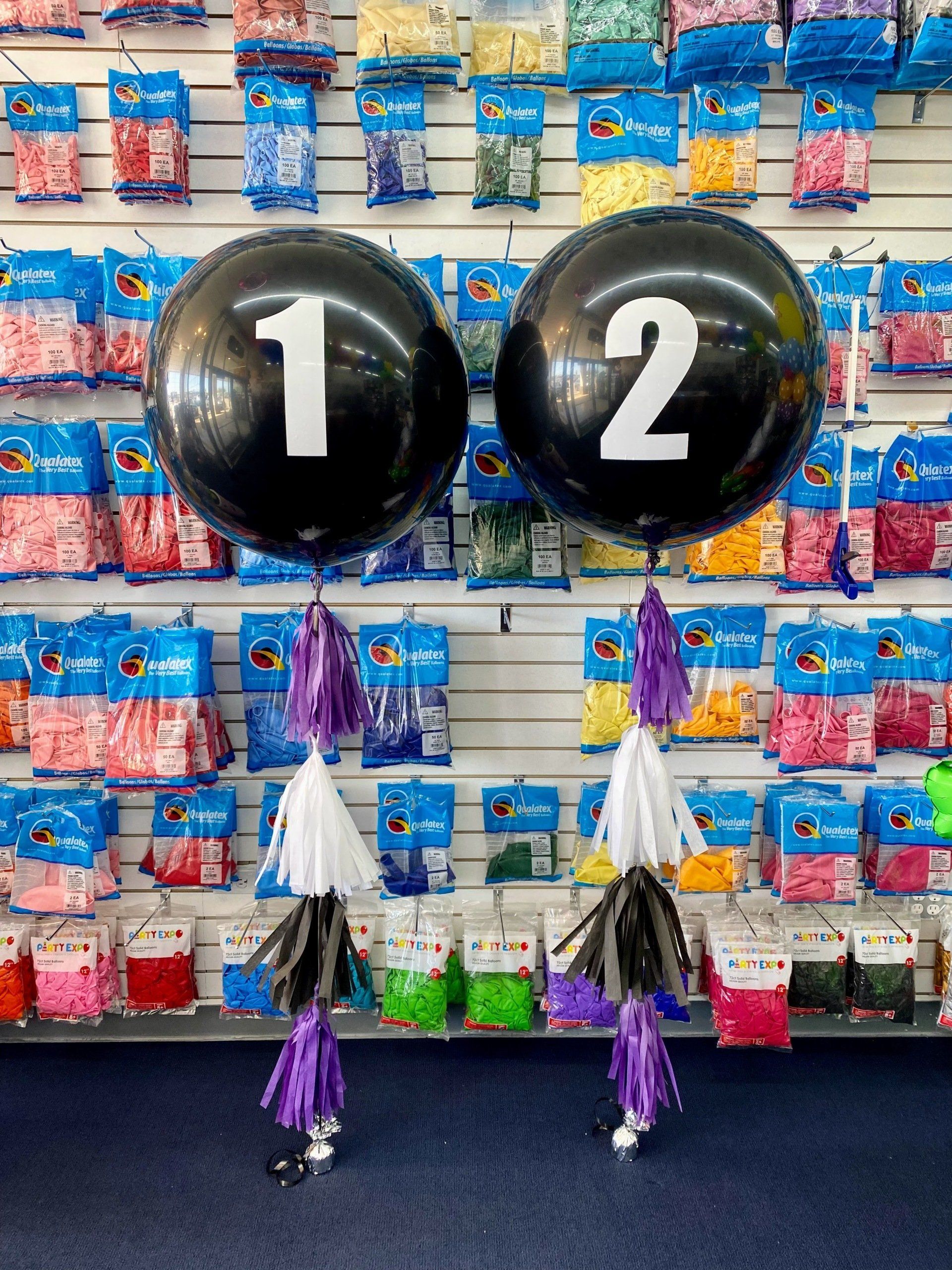 Two black balloons with the number 12 on them are sitting in front of a wall of balloons.