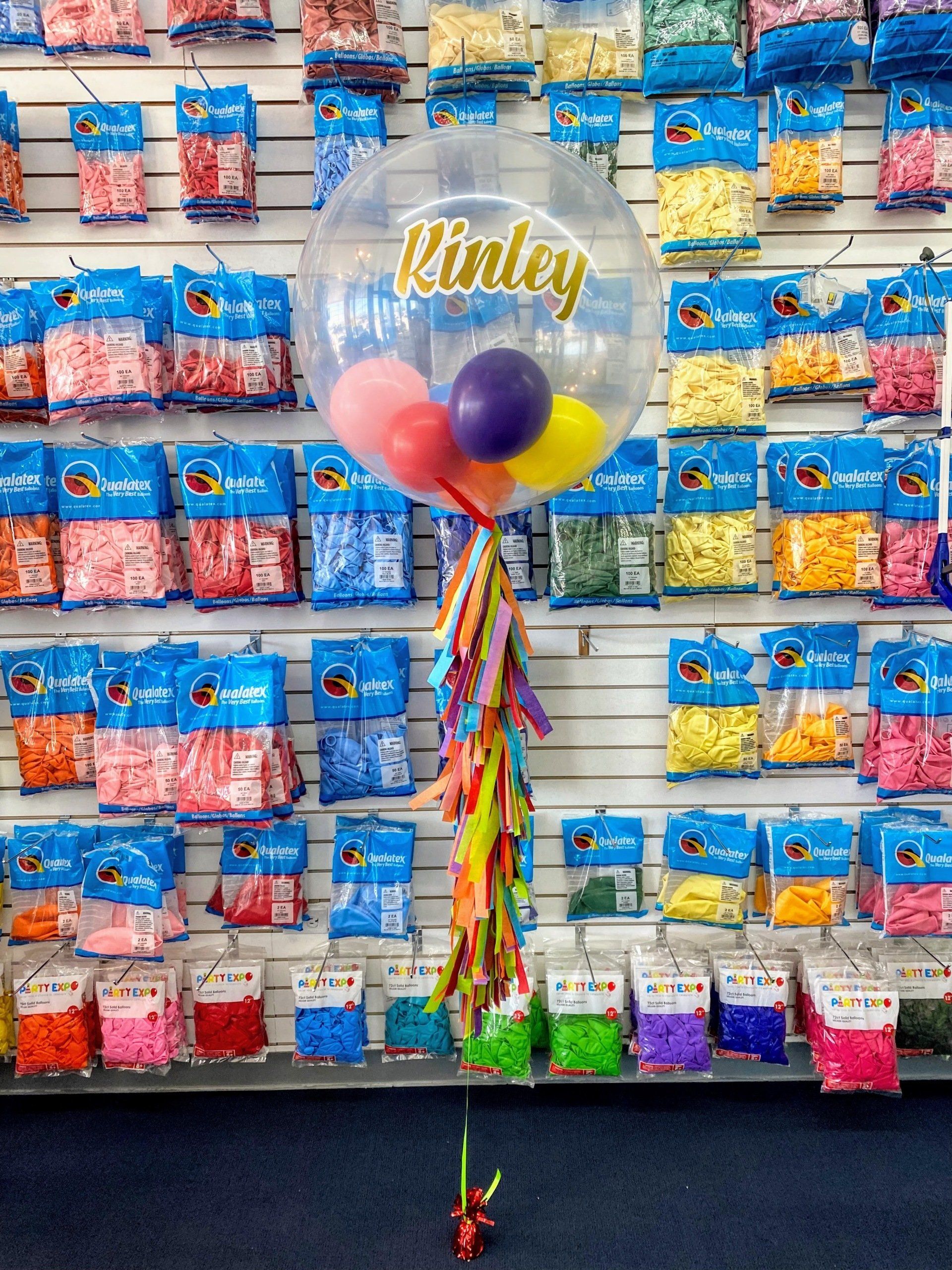 A clear balloon with a name on it is sitting in front of a wall of balloons.