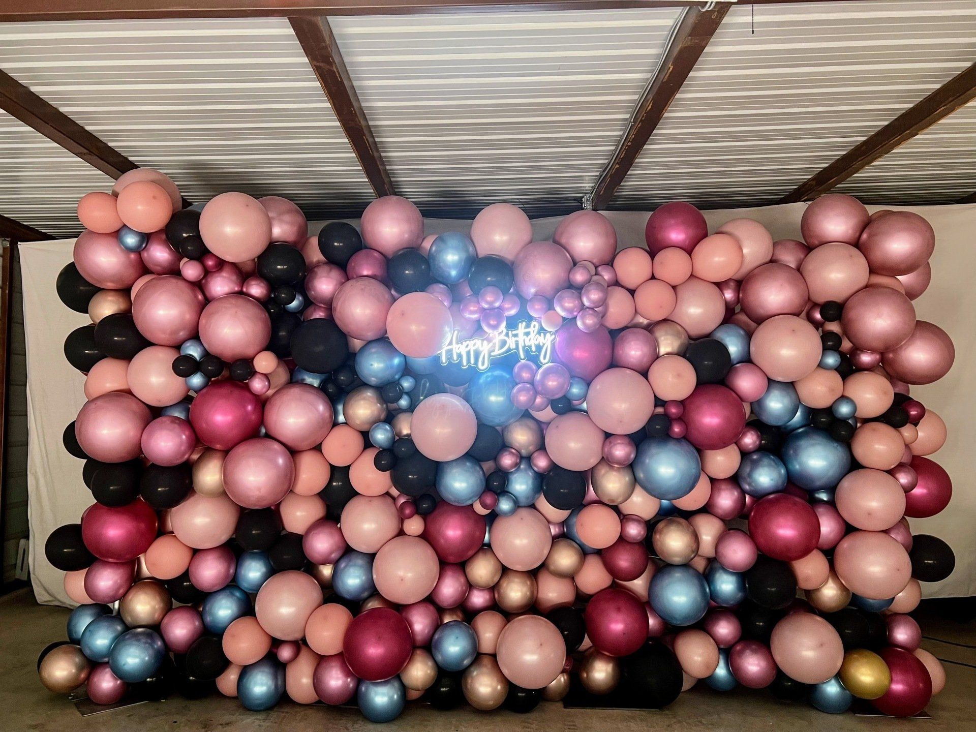A wall of balloons with a neon sign in the middle.