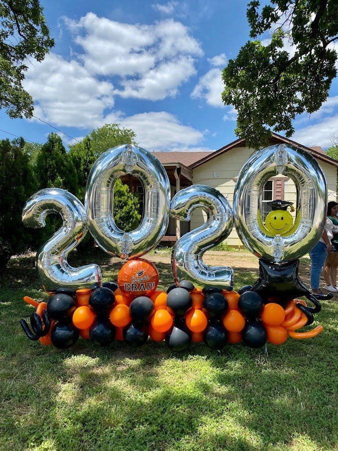 A bunch of balloons are sitting in the grass in front of a house.