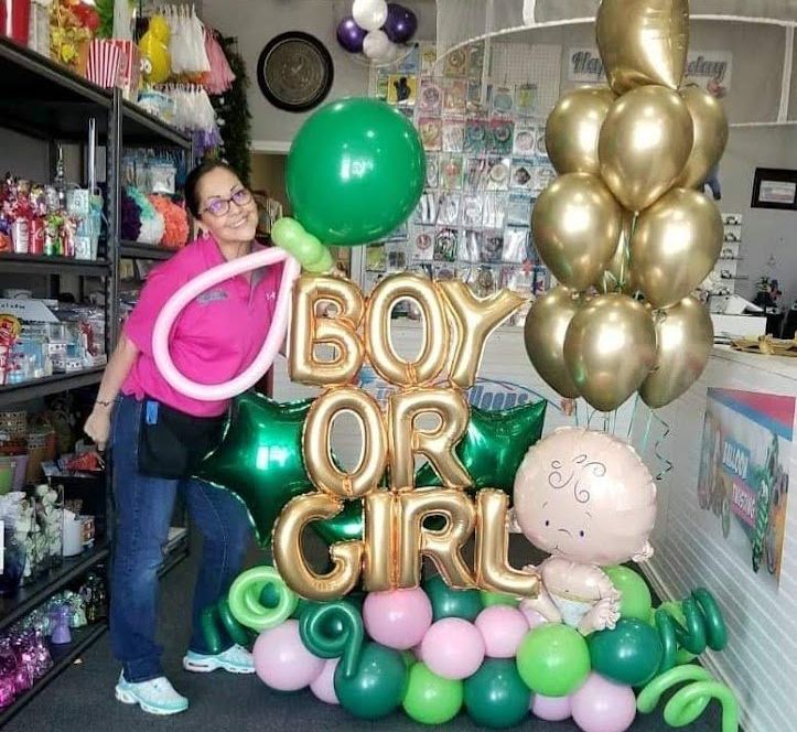 A woman is standing in front of a bouquet of balloons that says boy or girl.