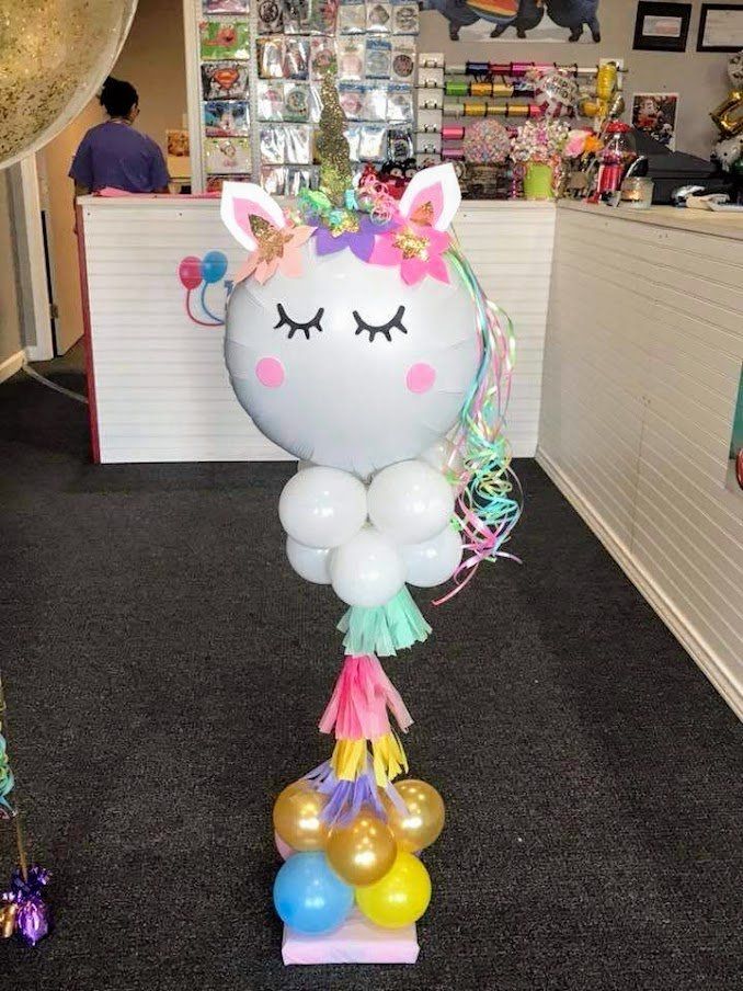 A unicorn balloon is sitting on top of a table with balloons.