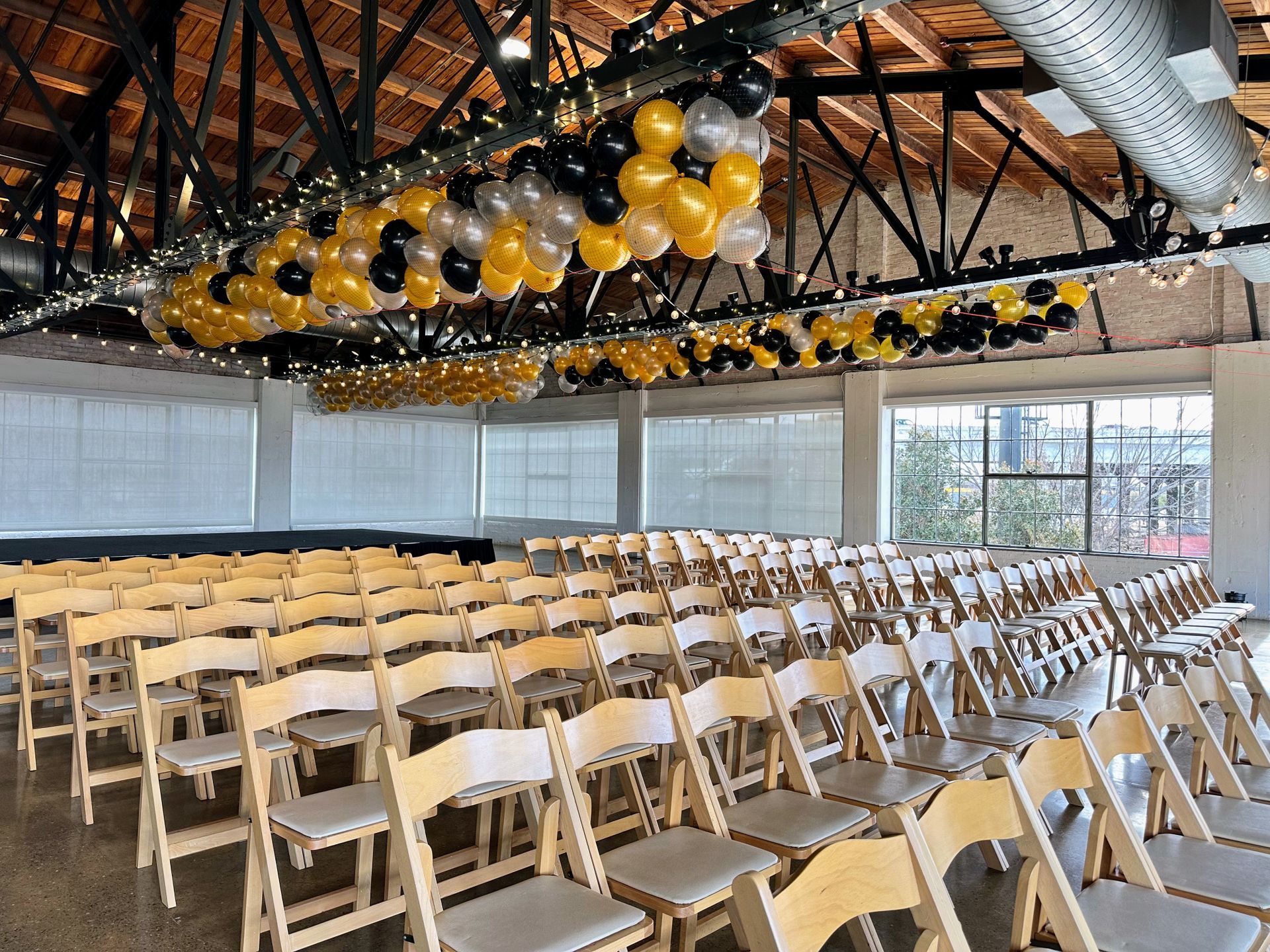 A room with rows of folding chairs and balloons hanging from the ceiling.