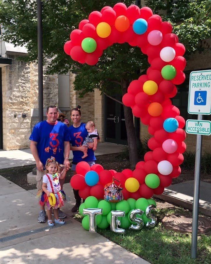 A group of people standing in front of a balloon arch that says tess