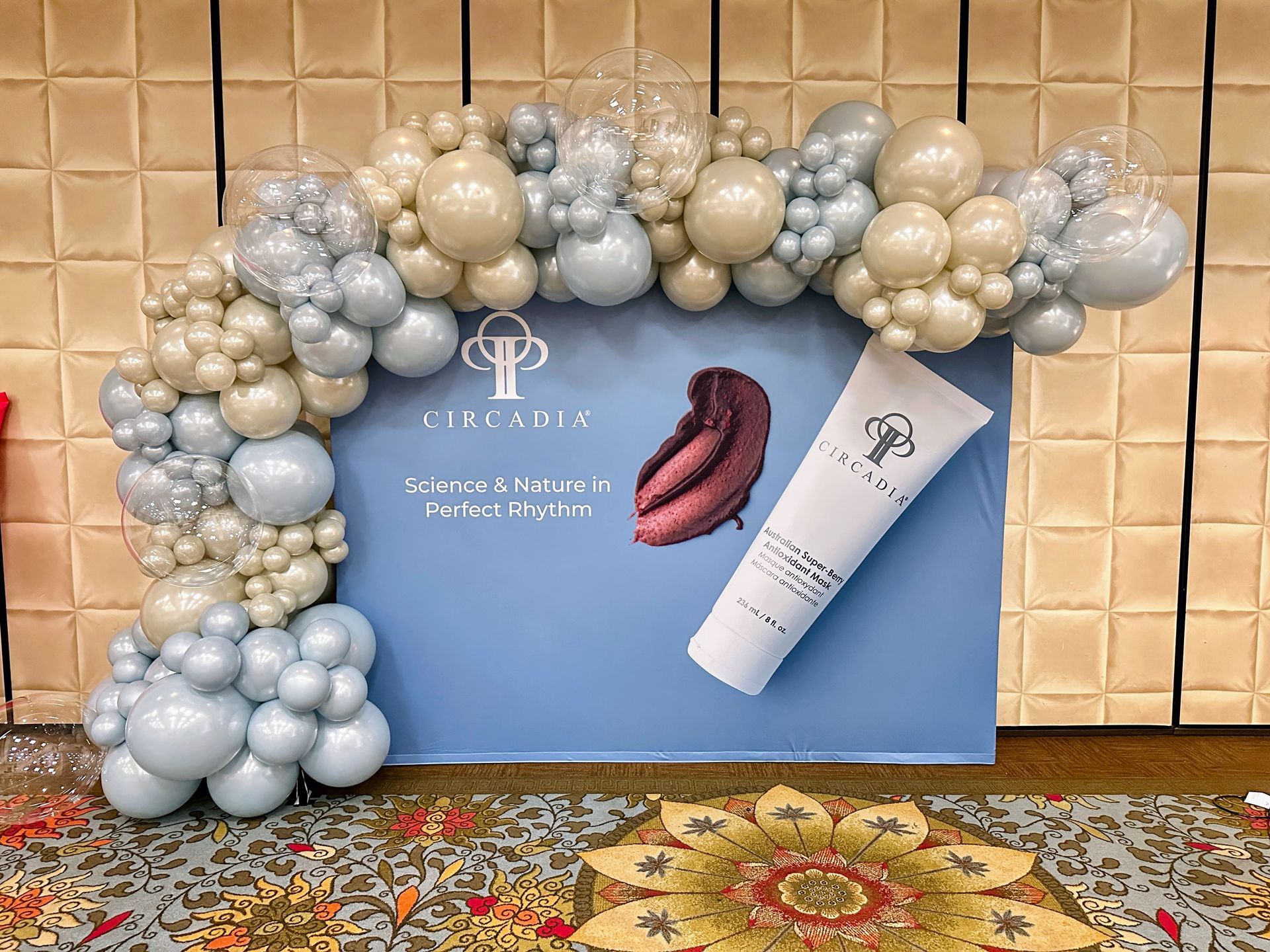 Luxury organic balloon backdrop in neutral beige and silver tones with branded display for corporate event