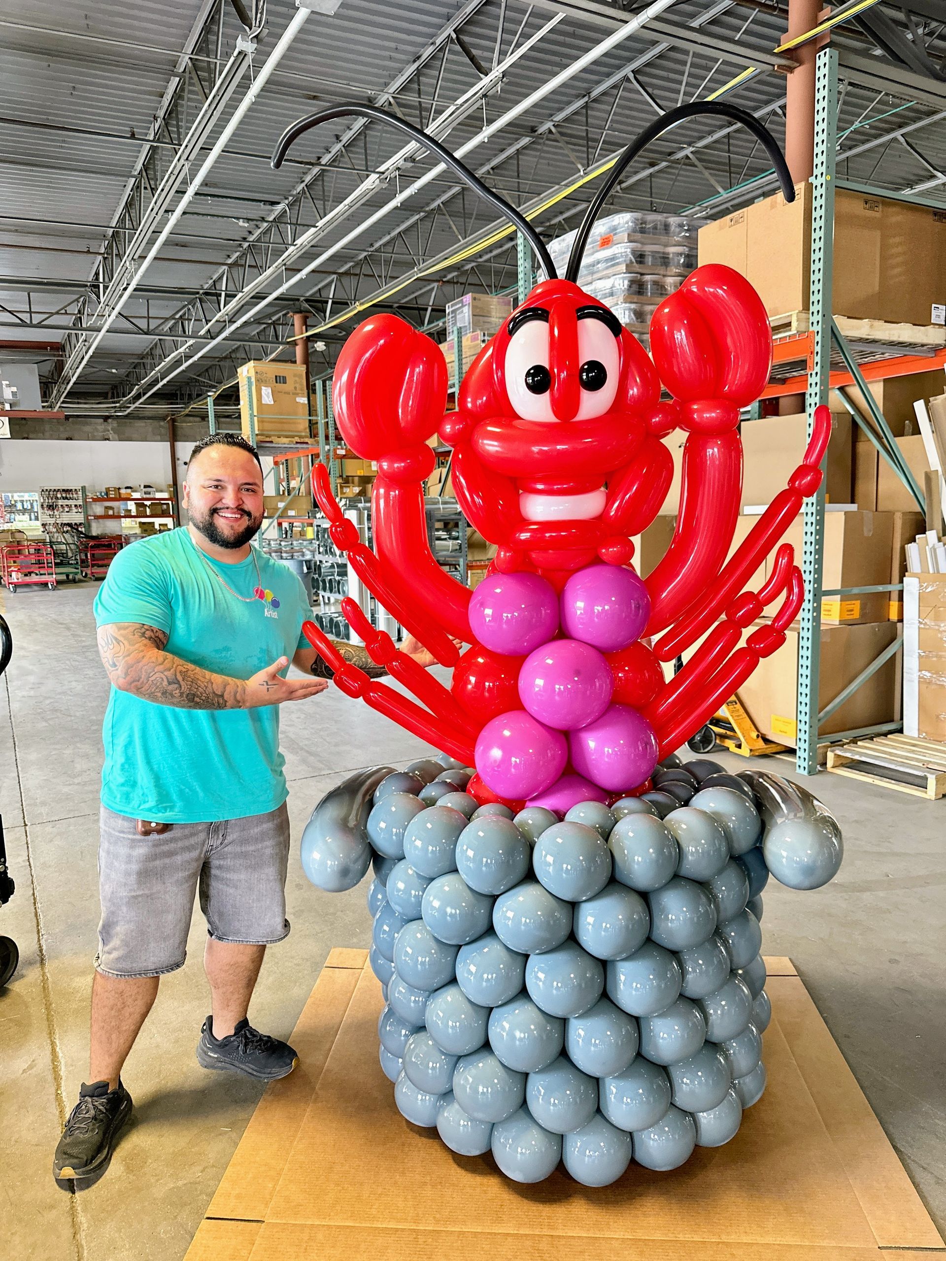 Balloon sculpture of a large crawfish  in a pot for a crawfish boil event with artist standing next to it.