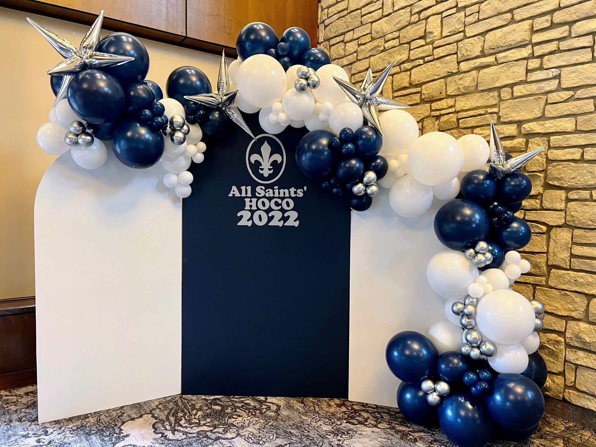 A blue and white balloon arch in front of a brick wall.
