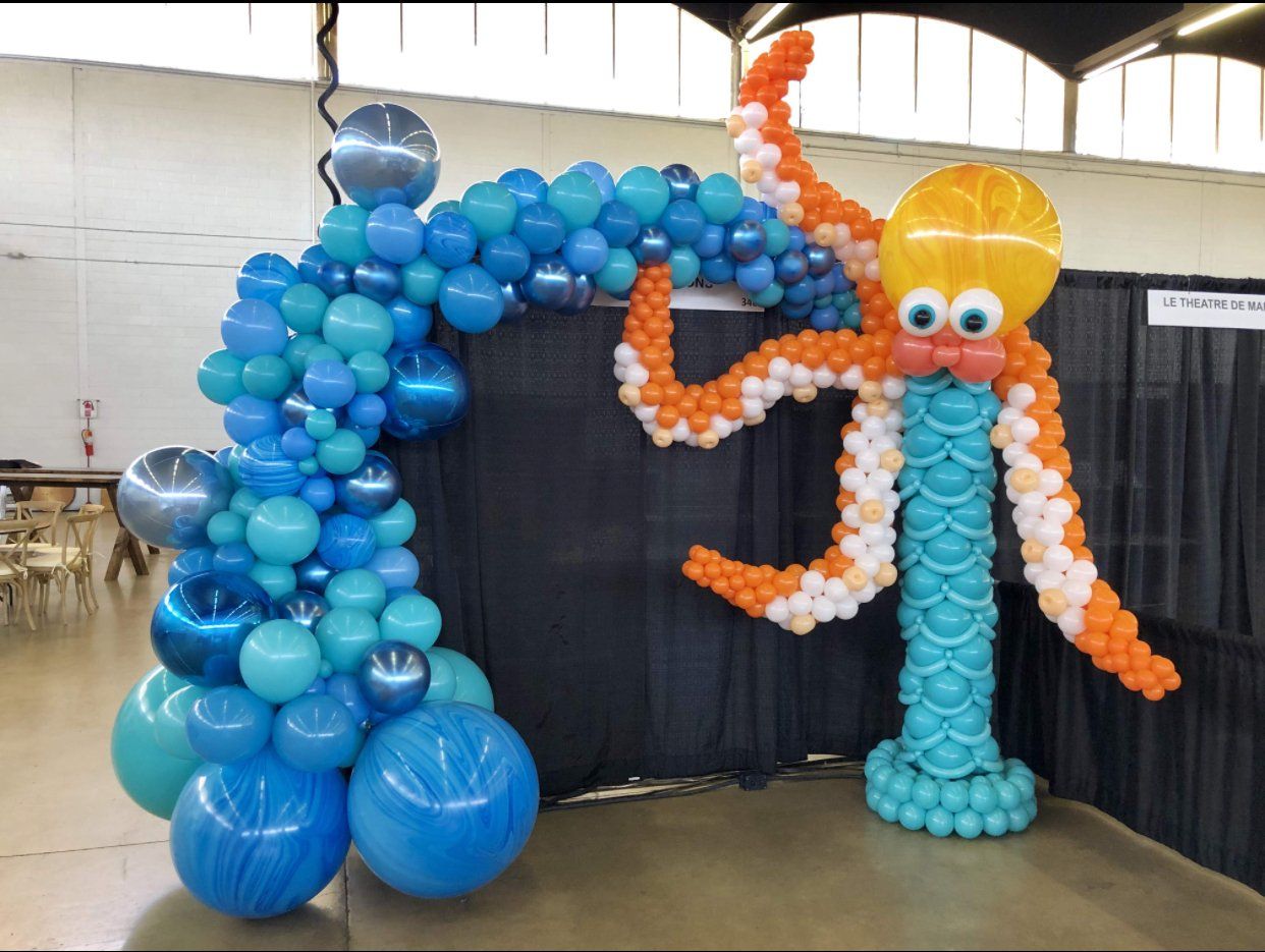 A balloon octopus is standing next to a balloon arch