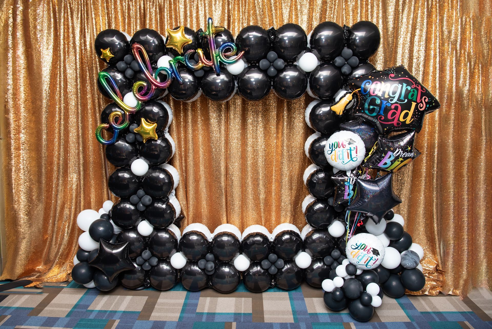 Black foil grad photo booth frame, 'Congrats Grad' letters, star balloons, black/gold backdrop. High school/college parties.