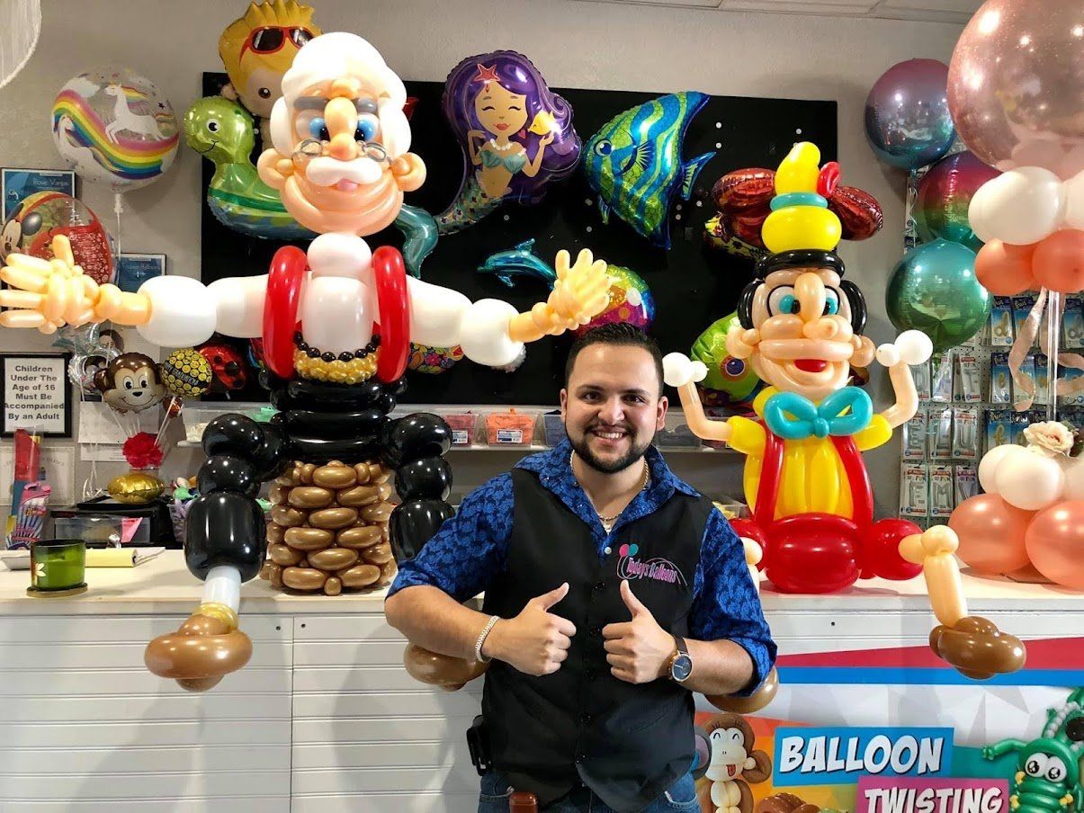 A man is standing in front of a bunch of balloons and giving a thumbs up.