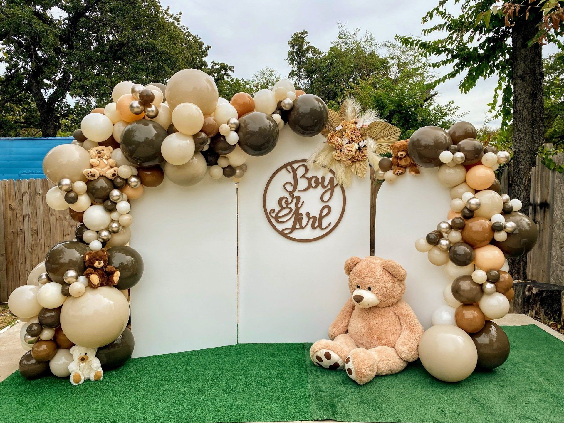 A teddy bear is sitting in front of a wall decorated with balloons.