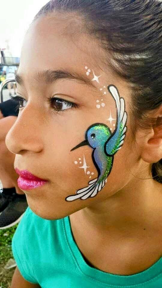 A young girl has a hummingbird painted on her face.