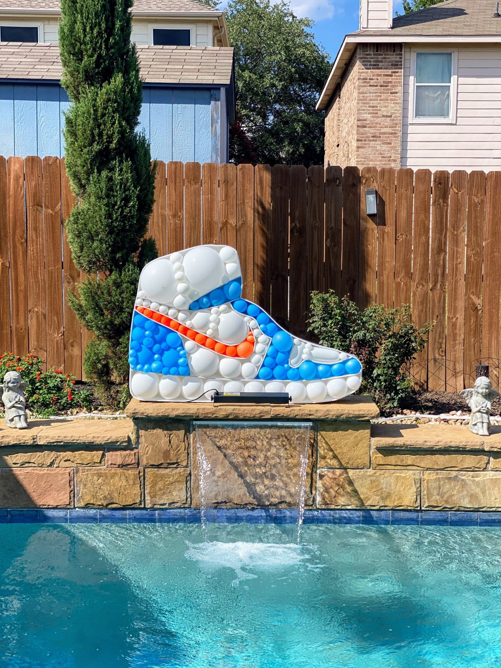 A giant nike shoe made of balloons is sitting next to a pool.