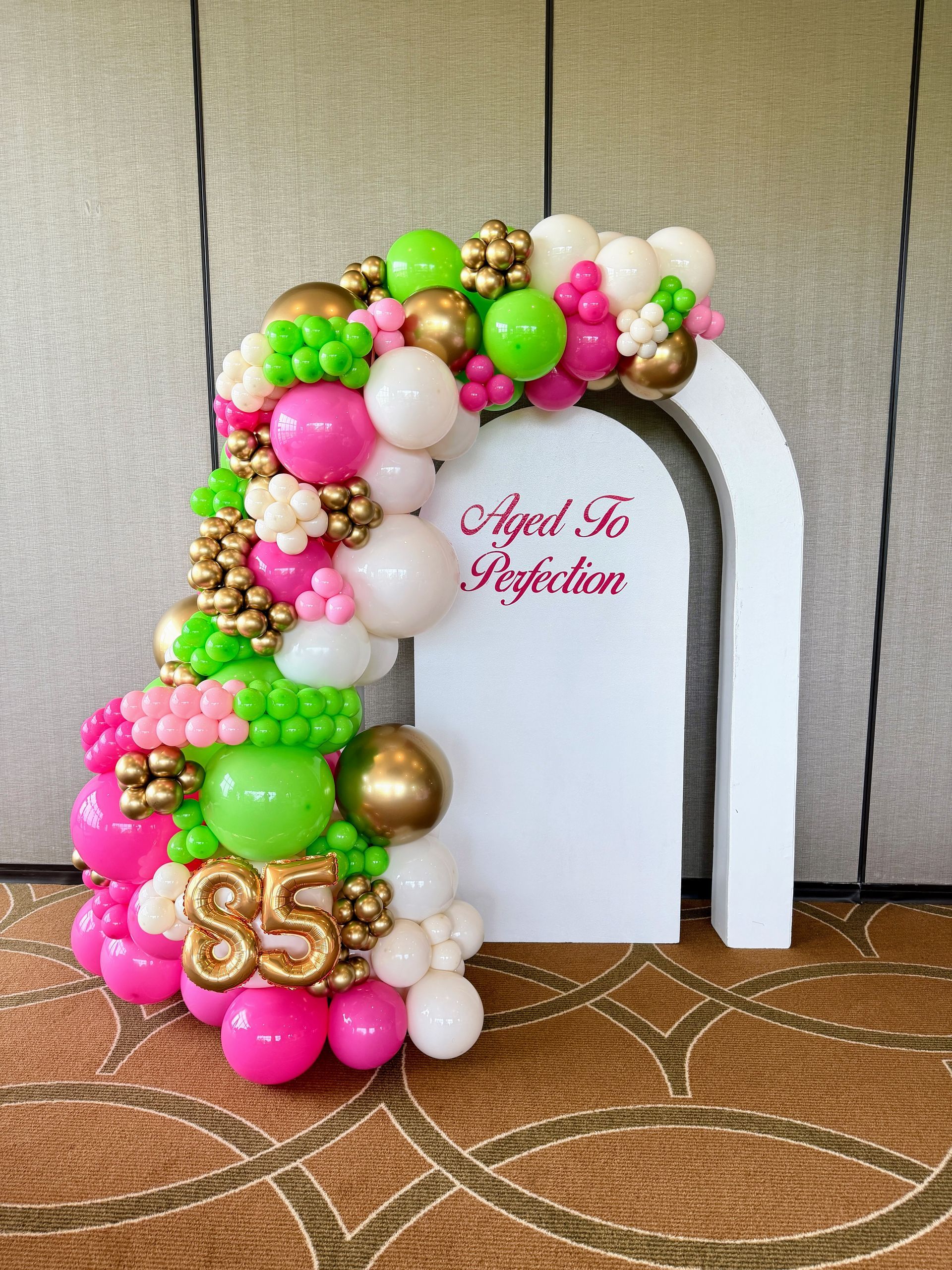 An elegant green, pink, and gold 85th birthday balloon garland with a white backdrop, personalized with vinyl.