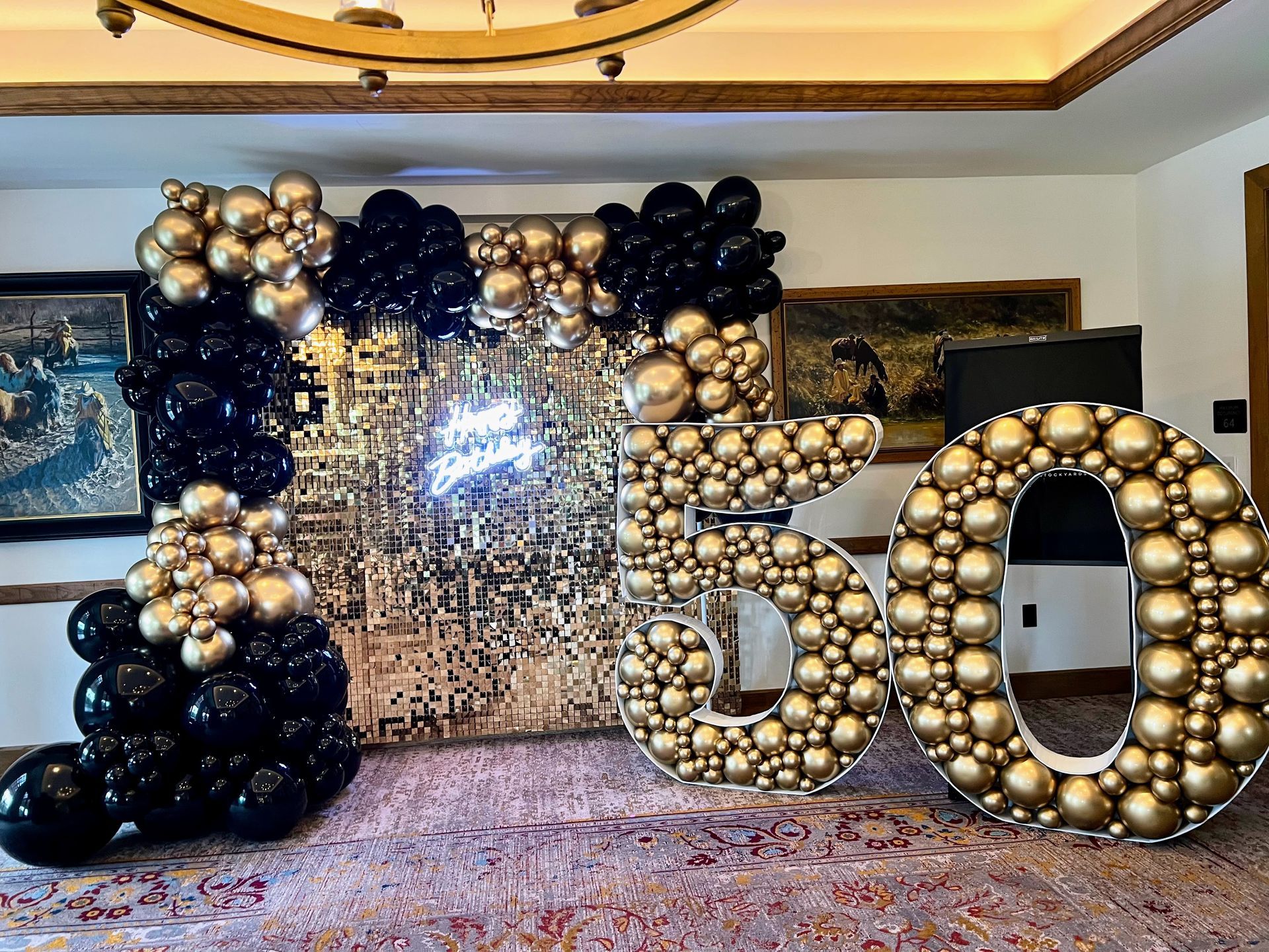 Elegant balloon garland featuring black and gold balloons styled with a gold shimmer wall backdrop